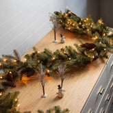 Decorative Christmas garland with lights and small ornaments on a wooden surface.
