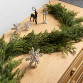 Decorative setup with greenery, deer figurines, and snowflake ornaments on a wooden surface.