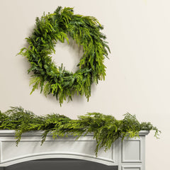 Green christmas wreath and garland on a white fireplace mantel against a beige wall.