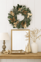 Christmas wreath with gold leaves and pinecones above a mirror on a desk