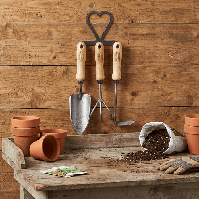 h potter dewit set of 3 Gardening tools on a wooden table with pots and soil against a wooden wall.