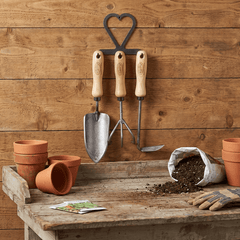 h potter dewit set of 3 Gardening tools on a wooden table with pots and soil against a wooden wall.