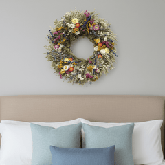Floral spring botanical wreath above a bed with pillows on a gray wall