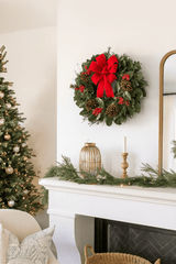 Christmas wreath with red bow on a mantelpiece with decorated tree and candles.