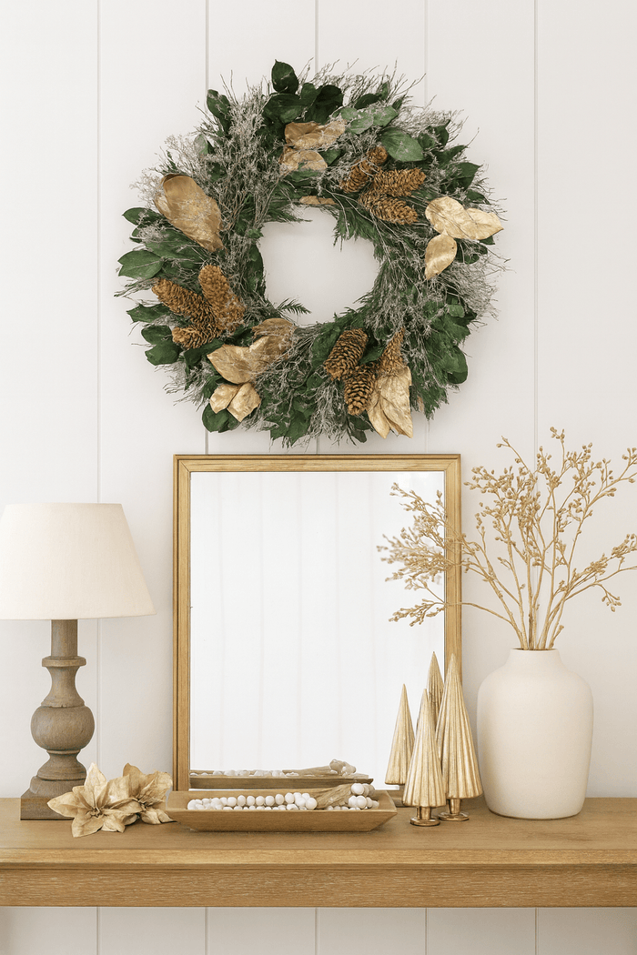 Christmas wreath with gold leaves and pinecones above a mirror on a desk