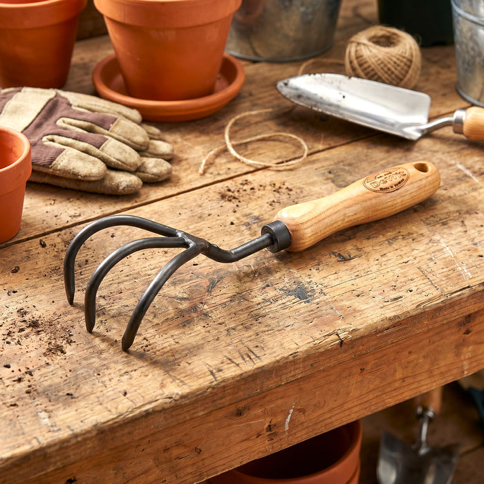 H Potter Dewit Gardening tool with wooden handle on a wooden workbench with pots and tools in the background.